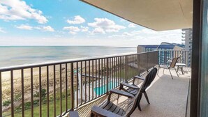 Un balcón con vistas a la playa y al océano, mobiliario exterior y una piscina.