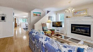 A living room with a sofa, television, fireplace, and artwork on the walls. - Savannahs Landing home w/ gas grill & shared pool, tennis, & playground (Ocean View)