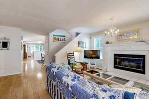 A living room with a sofa, television, fireplace, and artwork on the walls. - Savannahs Landing home w/ gas grill & shared pool, tennis, & playground (Ocean View)