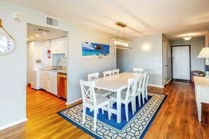 Un coin repas avec une table et des chaises, une cuisine en arrière-plan et un tableau accroché au mur.