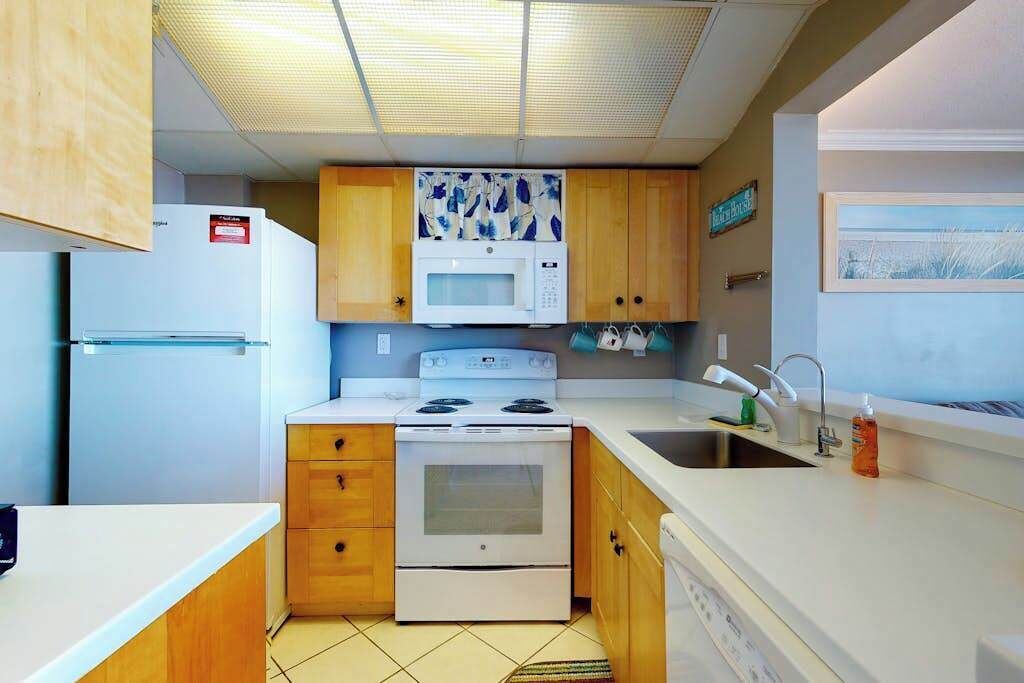 Een kleine keuken met houten kastjes, een magnetron, fornuis en een spoelbak.