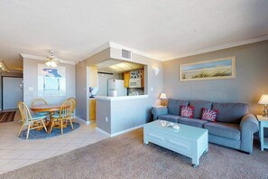 Ein Wohnzimmer mit grauem Sofa, einem Couchtisch, einem Essbereich mit Tisch und Stühlen, einer Küchenzeile mit Mikrowelle und einem Deckenventilator.
