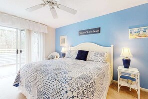 A bedroom with a bed, a ceiling fan, a nightstand with a lamp, a wall sign, and a window with curtains. - Sea Colony Tennis townhouse w/ shared pool and sauna, and free WiFi (Bethany Beach)