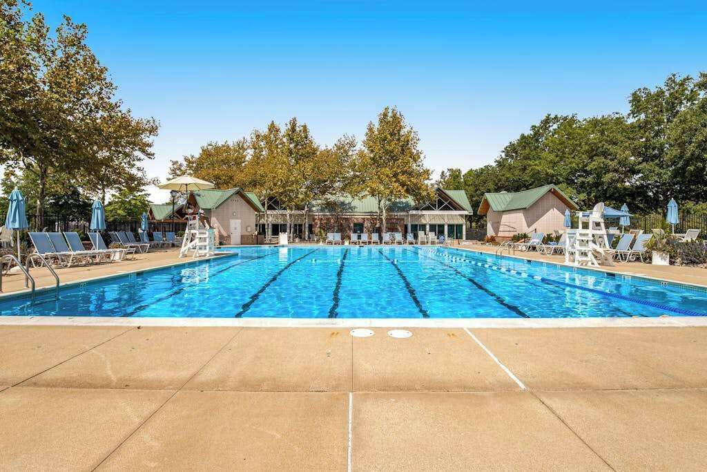 A swimming pool with multiple lanes, lounge chairs, and umbrellas, surrounded by trees and buildings.