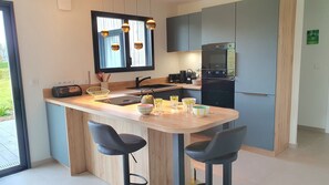 A modern kitchen with a central island, bar stools, a built-in oven, and a window with pendant lighting. - "Le Lodge Sainte Anne" open to the countryside (Sainte-Anne-d'Auray)