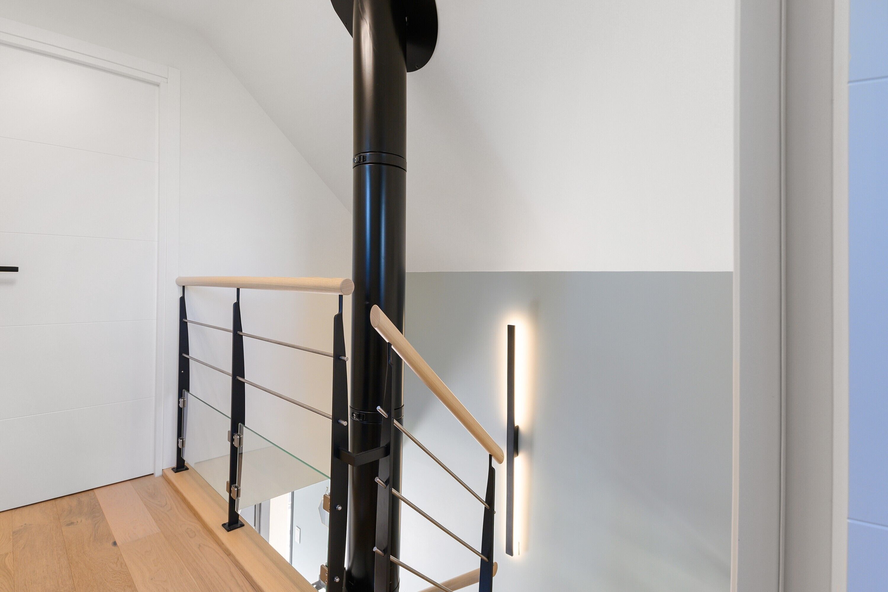 Un escalier moderne avec une main courante noire et des rampes en verre, menant à l’étage supérieur.