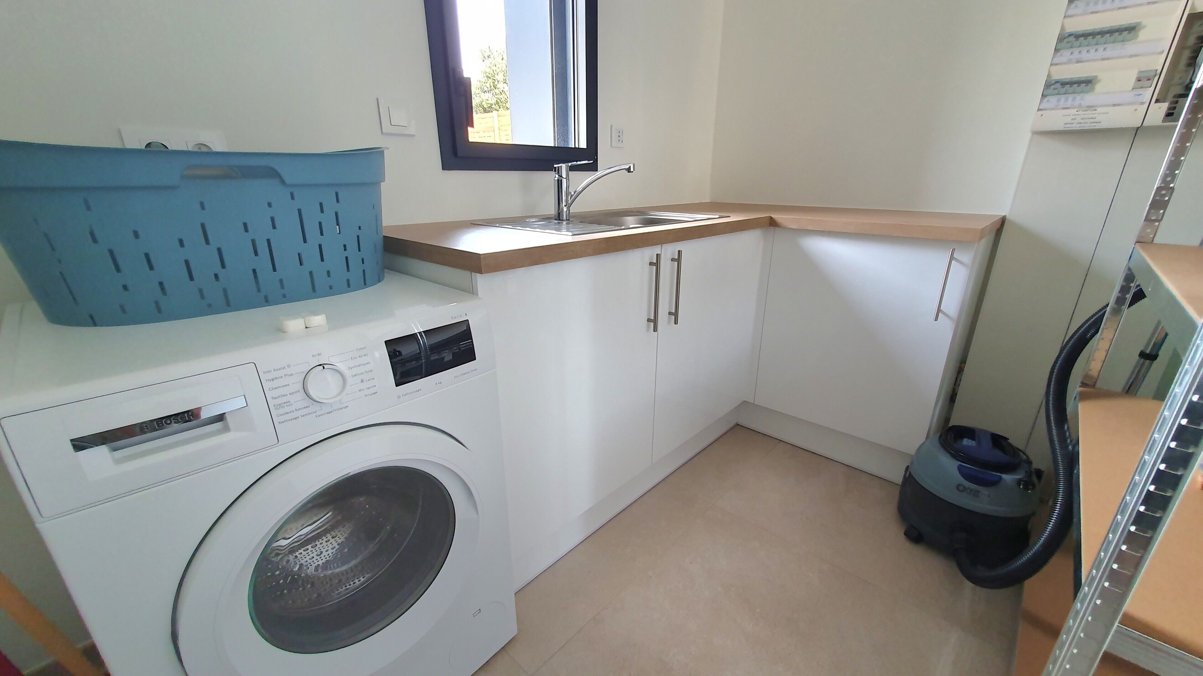 A compact laundry room with a washing machine, a sink, and a blue laundry basket.