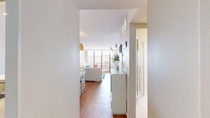 A narrow hallway leading to a kitchen with white cabinets and a dining area with a table and chairs. - Sea Colony Oceanside Condo Steps to Private Beach, Pools and Tennis (Bethany Beach)