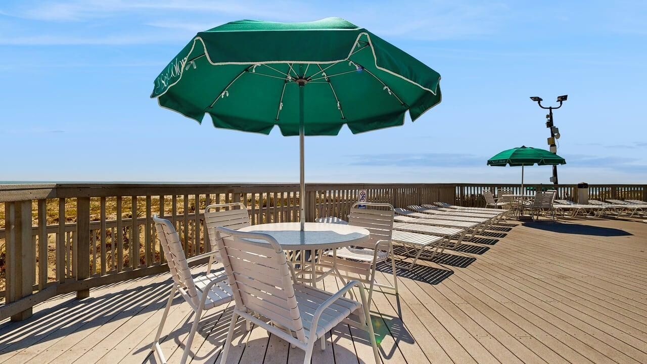 A wooden deck with a table and chairs, a green umbrella, and a railing.