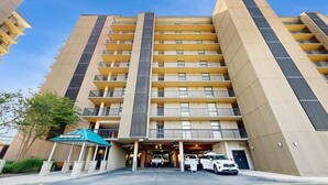 A multi-story hotel with a central entrance, balconies on each floor, and a parking area in front. - Sea Colony Oceanside Condo Steps to Private Beach, Pools and Tennis (Bethany Beach)