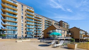 A multi-story hotel with balconies, a covered outdoor seating area, and a pool. - Sea Colony Oceanside Condo Steps to Private Beach, Pools and Tennis (Bethany Beach)