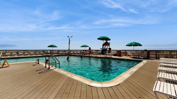 A pool area with a wooden deck, lounge chairs, and umbrellas. - Sea Colony Oceanside Condo Steps to Private Beach, Pools and Tennis (Bethany Beach)