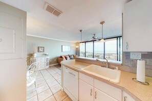 A kitchen with a dishwasher, a sink, and a window overlooking a balcony.