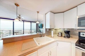 A modern kitchen with white cabinets, a large window, and a balcony.