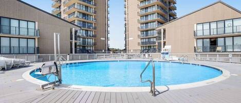 A swimming pool surrounded by a wooden deck, with two high-rise buildings in the background.