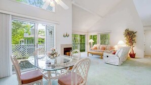 A spacious living area with a glass dining table, white furniture, and a ceiling fan. - Terrific Sea Colony Condo w/Private Beach, Free WiFi, Shared Pool & Hot Tub, AC (Bethany Beach)