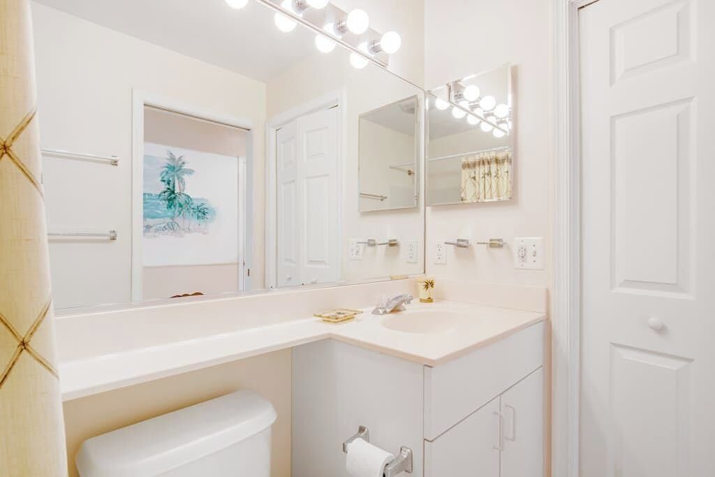 A bathroom with a white vanity, a large mirror with lights, a toilet, and a towel rack.