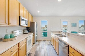 A modern kitchen with wooden cabinets, stainless steel appliances, and a view of the city. - Villas at Beach Cove Getaway W/ Bay/Ocean Views, Private Balcony & Shared Pool (Bethany Beach)