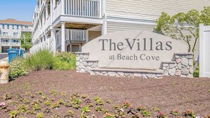 Een bordje voor 'The Villas at Beach Cove', met een stenen voet en een wit gebouw op de achtergrond.