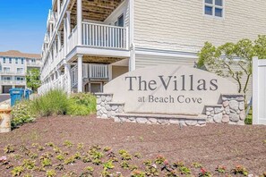 A sign for 'The Villas at Beach Cove' with a stone base and a white building in the background. - Villas at Beach Cove Getaway W/ Bay/Ocean Views, Private Balcony & Shared Pool (Bethany Beach)