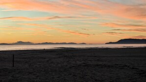 Une plage avec un ciel au coucher du soleil, des montagnes lointaines et un rivage sablonneux.