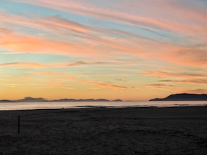 Una spiaggia con un cielo al tramonto, montagne in lontananza e una battigia sabbiosa.