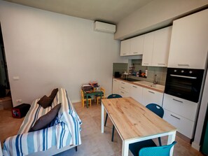 Un pis petit i modern amb cuina americana, un sofà amb ratlles, una taula de dinar de fusta i una taula petita a la cuina.