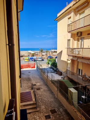 Vista des d'un balcó sobre un carrer pavimentat, amb un cel blau clar i una platja allunyada.