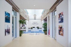 A modern lobby with a reception desk, a sign reading 'Welcome to the Health Aquatic Club,' and a glass wall on one side. - Bayside Condo w/ Balcony & Amazing Shared Pools, Hot Tub, Golf, Tennis, Fitness (Selbyville)