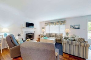Ein Wohnzimmer mit Kamin, gestreiften Sofas, einem Fernseher und einem Fenster mit Jalousien.