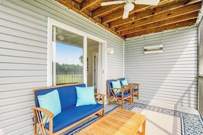 Une véranda couverte avec un ventilateur de plafond, une table en bois et deux chaises en bois dotées de coussins.