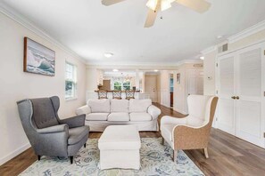Un salon avec un fauteuil gris, un canapé blanc et un tapis à motifs.