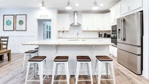 Een moderne keuken met witte kasten, roestvrijstalen apparatuur en een centraal eiland met barkrukken.