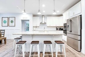 A modern kitchen with white cabinets, stainless steel appliances, and a central island with bar stools. - Bethany West Retreat W/ Shared Pool, Free WiFi, Full Kitchen & Ideal Location (Bethany Beach)