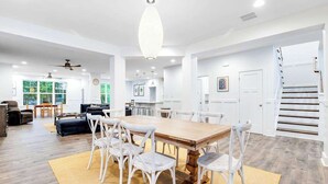 Een ruime woonkamer met een grote houten eettafel, witte stoelen en een kroonluchter.