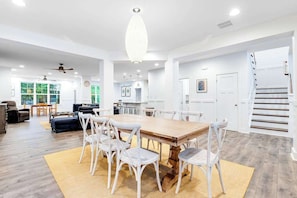 A spacious living room with a large wooden dining table, white chairs, and a chandelier. - Bethany West Retreat W/ Shared Pool, Free WiFi, Full Kitchen & Ideal Location (Bethany Beach)