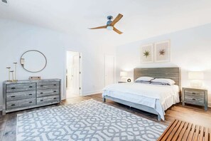 Une chambre à coucher comprenant un lit, des tables de chevet, un ventilateur de plafond, un tapis à motifs et un banc en bois.