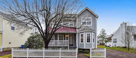 A two-story house with a porch, a tree in front, and a white picket fence.