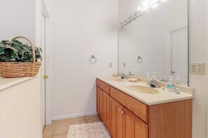 Un baño con tocador de madera, dos lavamanos, un espejo grande y una cesta con plantas verdes.