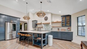 A modern kitchen with a central island, bar stools, a stainless steel refrigerator, and pendant lighting. - Luxury Villa: Pool, Hot Tub & Fire Pit Near Strip (Las Vegas)