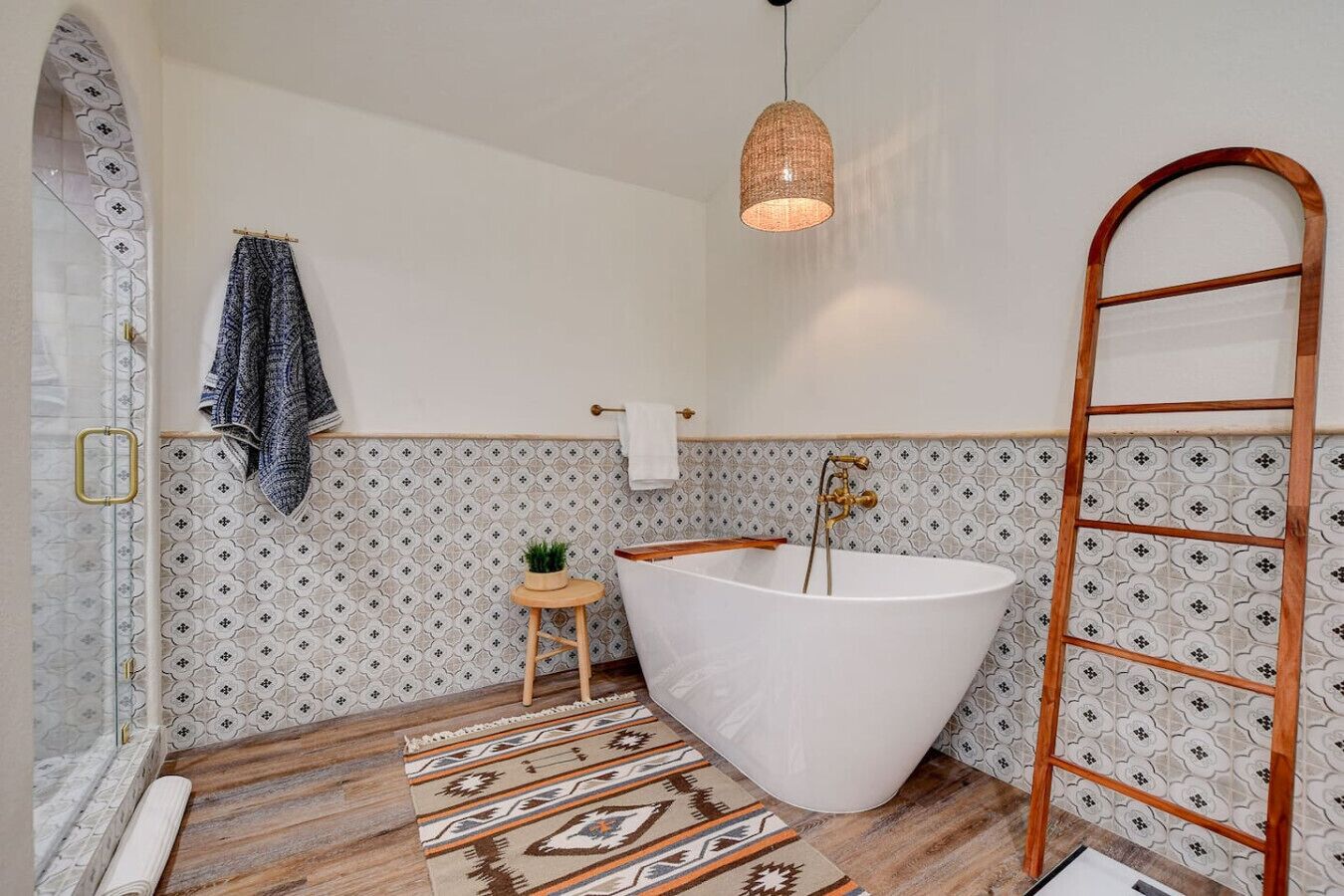 A bathroom with a freestanding bathtub, a wooden ladder, a hanging light fixture, and patterned tiles.