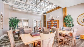Ein geräumiges Zimmer mit hoher Decke, einem großen Bücherregal und zwei Topfpflanzen.