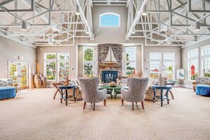 A spacious room with a stone fireplace, large windows, and a high ceiling with exposed beams. - Bethany Lakes townhome with fireplace, balcony, & community pool/hot tub/tennis (Ocean View)