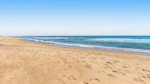 Een zandstrand met voetafdrukken, een heldere lucht en rustige golven.