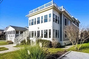 A two-story house with a covered porch, a staircase, and a well-maintained lawn. - Town of Bethany beach house with expansive rooftop deck & several kitchens (Bethany Beach)