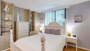 Une chambre à coucher comprenant un lit, des tables de chevet, une commode, une lampe, une étagère avec des objets décoratifs, une horloge murale et une fenêtre avec des rideaux.
