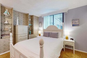 Ein Schlafzimmer mit Bett, Nachttischen, einer Lampe, einem Regal mit Dekoration, einer Wanduhr und einem Fenster mit Vorhängen.