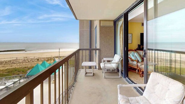 Un balcon avec vue sur la plage, un coin salon avec des meubles blancs, et une chambre avec un lit et une fenêtre.