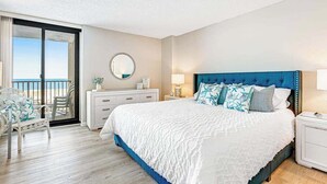 Ein Hotelzimmer mit einem großen Bett, einem Balkon mit Blick, einem runden Spiegel und einer weißen Kommode.