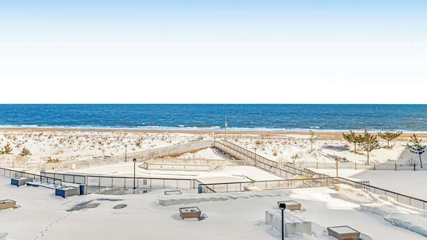 Ein Strandhotel mit verschneiter Terrasse, Poolbereich und Blick auf den Ozean.